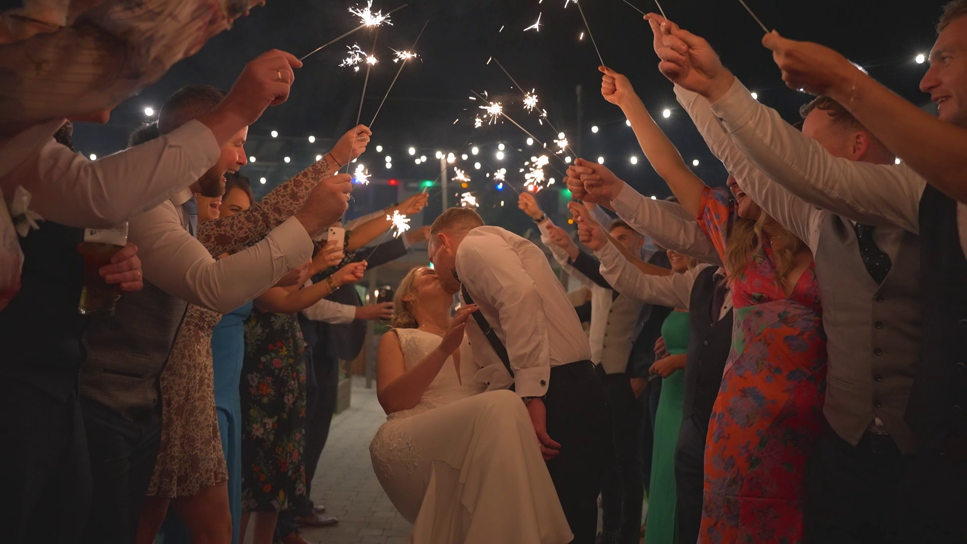 A newlywed couple kissing under the light of guests sparklers